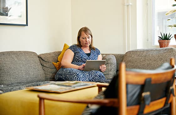 Kvinna sitter uppkrupen i en soffa och använder Ipad. 