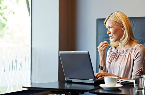 Kvinna pratar i headset i en mobiltelefon. Hon sitter framför en laptop med en kopp kaffe i förgrunden.