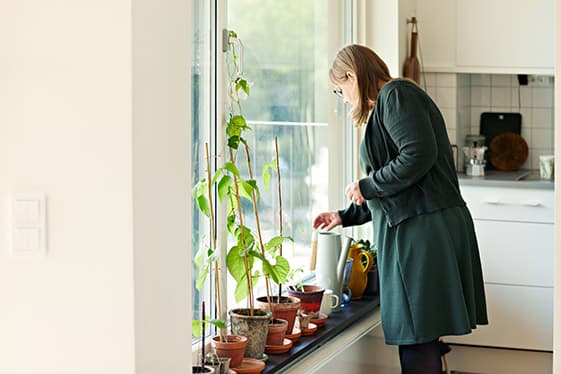 Kvinna pysslar med krukväxter i ett fönster i sitt hem