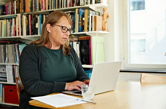 Yngre kvinna sitter vid en dator och tittar bort. I bakgrunden diskuterar kollegor. 